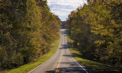 A winding road stretches through a tree-lined landscape under a partly cloudy sky.