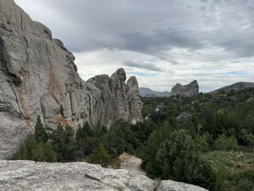 A rocky landscape with towering cliffs and lush greenery under a cloudy sky.