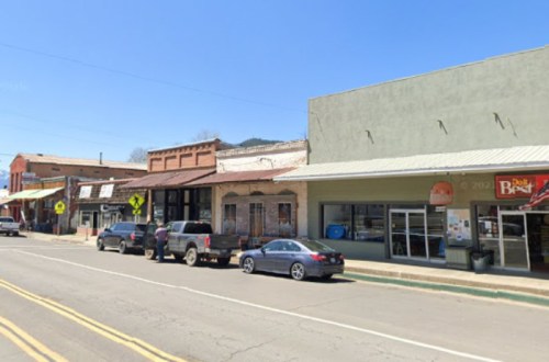 A small town street with shops, parked cars, and clear blue skies.