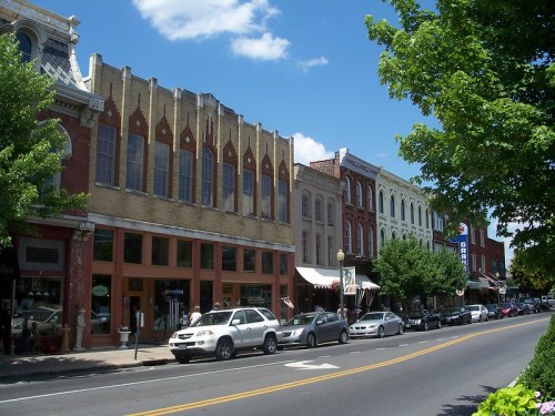 A charming street lined with historic buildings, shops, and trees under a blue sky with fluffy clouds.