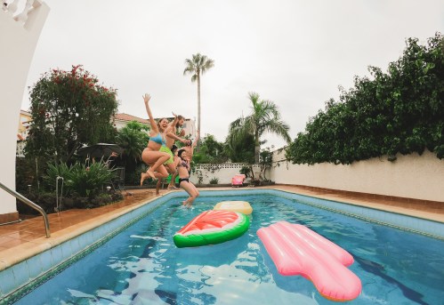 Group of multiracial friends jumping into a pool on summer vacation, with focus on the smiling face of the girl on the left.