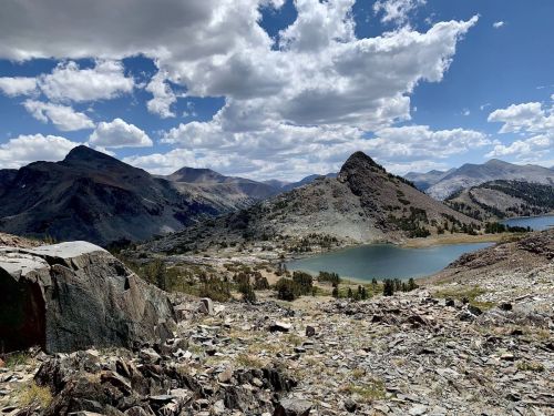 A scenic mountain landscape featuring rocky terrain, a lake, and dramatic clouds in a blue sky.