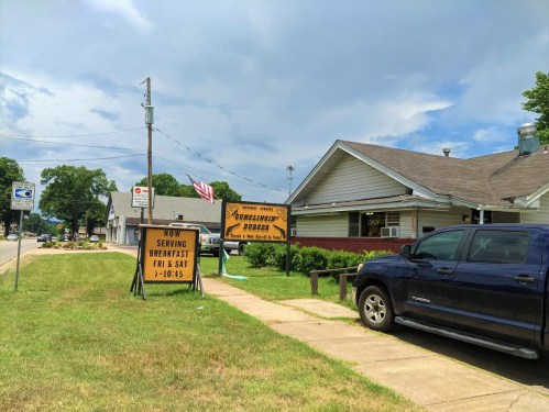 A roadside view of a restaurant with a sign announcing breakfast hours, alongside a parked blue truck.