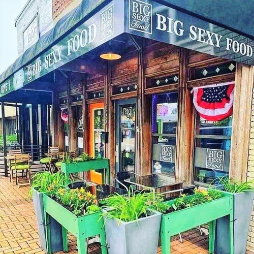 Exterior of a restaurant named "Big Sexy Food," featuring outdoor seating and planters with greenery.