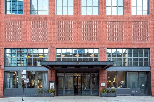 A modern brick building with large windows and a glass entrance, featuring urban landscaping in front.