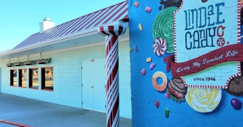 Colorful exterior of a candy shop featuring a mural of sweets and a striped pole, with a blue wall and red roof.