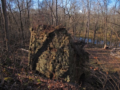 Ruins of a stone structure covered in moss, surrounded by bare trees and a calm river in the background.