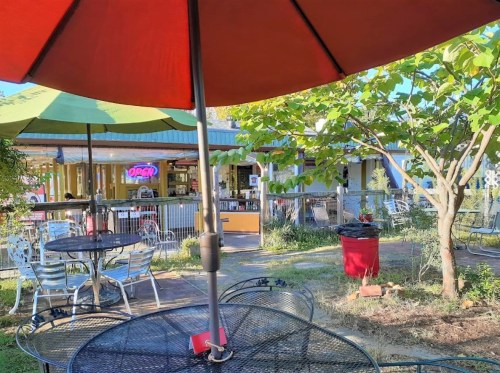 Outdoor dining area with tables under colorful umbrellas, featuring a vibrant restaurant in the background.