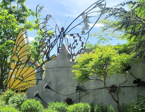 A large, colorful butterfly sculpture surrounded by greenery and trees under a clear blue sky.