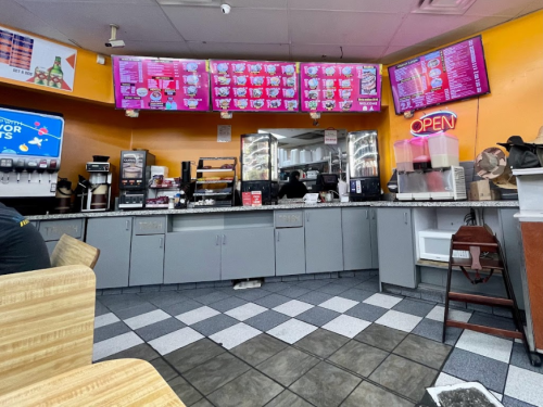 Interior of a fast-food restaurant with a colorful menu board, open sign, and seating area.