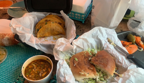 A table with tacos, a sandwich, a bowl of soup, and assorted vegetables, all wrapped in paper.