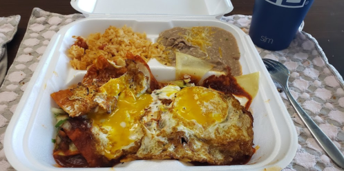 A takeout container with rice, refried beans, and a dish topped with eggs and sauce.