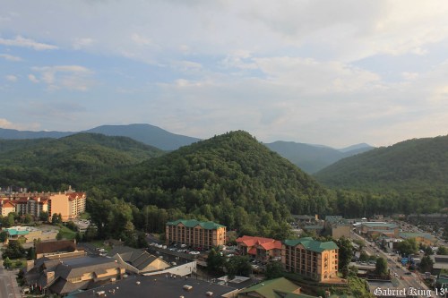 A scenic view of green mountains and a small town with hotels under a cloudy sky.