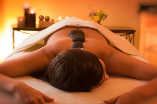 A person receiving a massage with smooth stones placed on their back, surrounded by a warm, calming atmosphere.