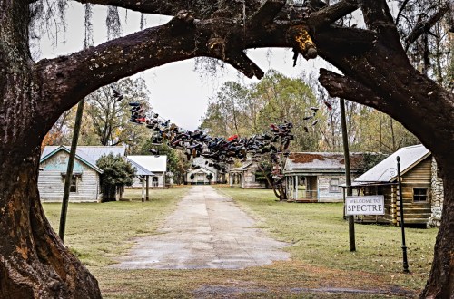 A view through an archway of a deserted street lined with old houses, with shoes hanging above the path.