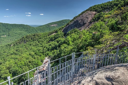 A scenic view from a rocky overlook, showcasing lush green mountains and a clear blue sky.