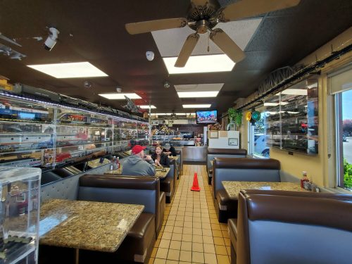 Interior of a diner with train memorabilia, featuring booths, a TV, and patrons enjoying their meals.