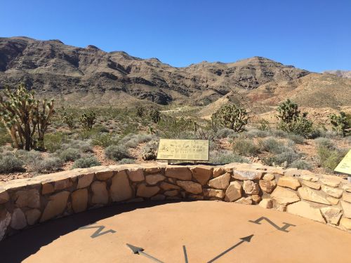 Desert landscape with mountains in the background, featuring a stone viewing platform and directional markers.