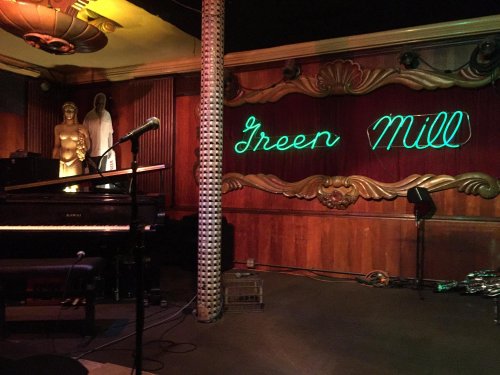 Interior of the Green Mill, featuring a piano, microphone, and neon sign against a vintage backdrop.