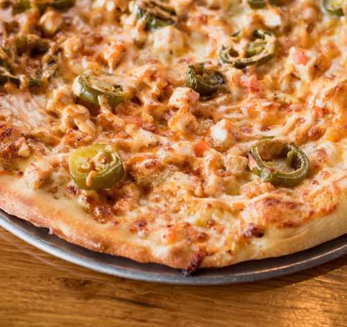 A close-up of a pizza topped with cheese, jalapeños, and bits of meat on a wooden table.