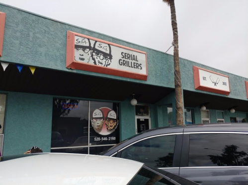 Exterior of a restaurant called "Serial Grillers," featuring a colorful sign and palm trees in the background.