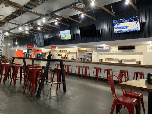 A modern restaurant interior with high tables, red stools, and multiple TVs showing sports.