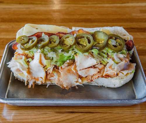 A sub sandwich filled with shredded chicken, lettuce, jalapeños, and cheese on a toasted hoagie roll.