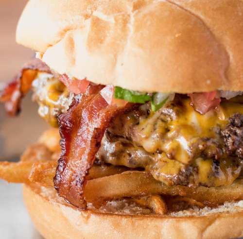 A close-up of a juicy cheeseburger with bacon, lettuce, and a soft bun, served with crispy fries on the side.
