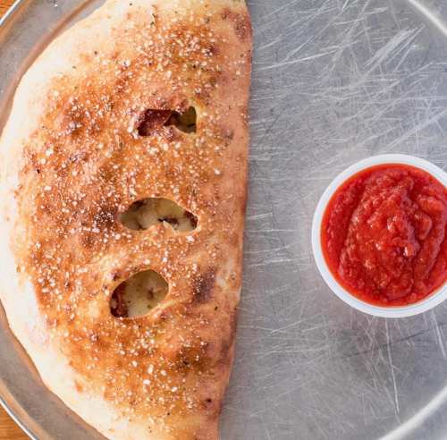 A golden-brown calzone with three openings, served on a plate with a small bowl of marinara sauce.