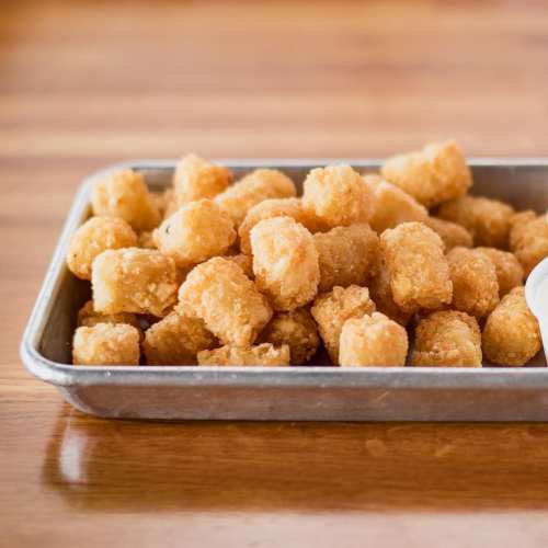 A metal tray filled with golden, crispy tater tots on a wooden surface.