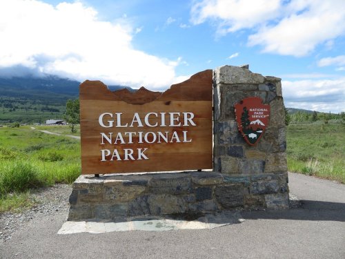 Sign for Glacier National Park, featuring a wooden structure and a park emblem, set against a scenic landscape.