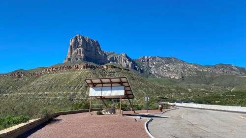 A scenic view of a mountain with a clear blue sky, featuring a roadside information shelter in the foreground.