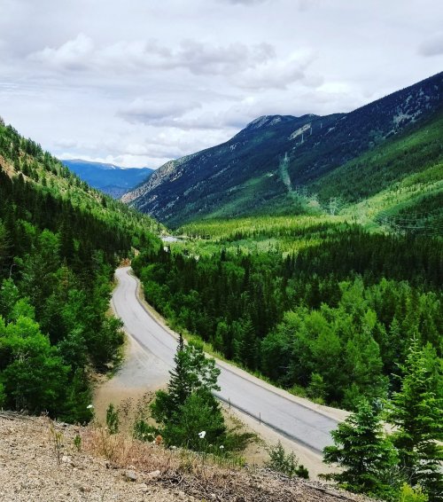 A winding road through lush green mountains under a cloudy sky, showcasing a scenic valley view.
