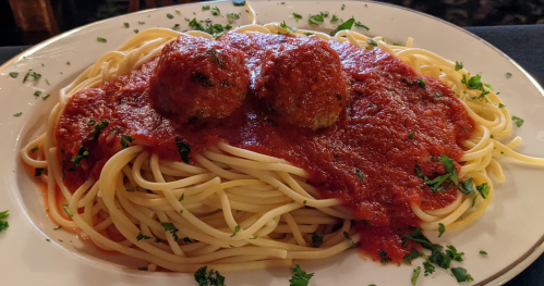 A plate of spaghetti topped with marinara sauce and two meatballs, garnished with parsley.