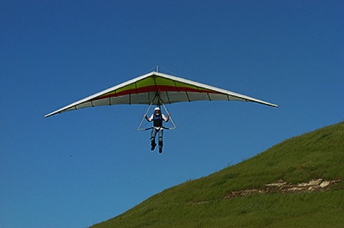 A person hang gliding above a green hillside against a clear blue sky.