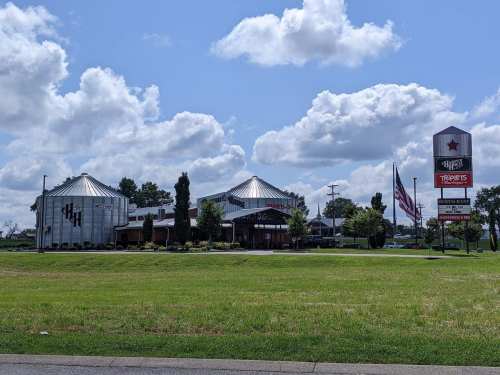 A restaurant with a modern design, featuring silos, an American flag, and a sign with various dining options.