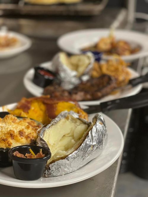 A plate of food featuring a baked potato, mac and cheese, and a side of meat, with dipping sauces in small containers.