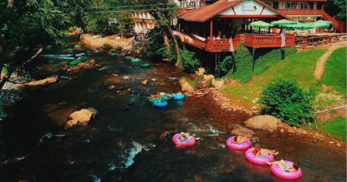 A group of people tubing on a lazy river in Helen, Georgia, surrounded by a scenic creek and woodlands.