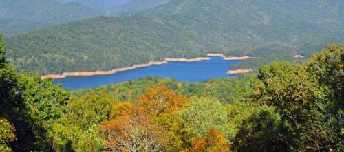 A scenic view of a lake surrounded by lush green mountains and autumn-colored trees.