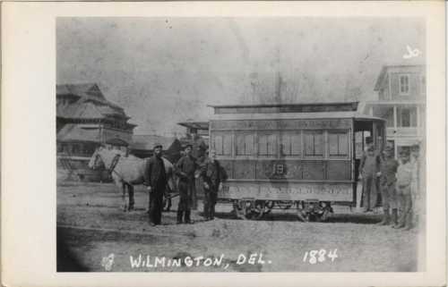 Historic photo of a horse-drawn streetcar in Wilmington, Delaware, from 1884, with men standing beside it.