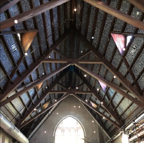 Interior view of a library with a wooden ceiling, featuring bookshelves and artistic decorations.