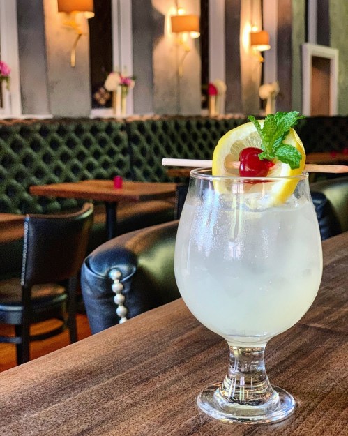 A refreshing cocktail with a lemon slice and cherry, served in a glass on a wooden table in a stylish bar setting.