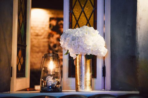 A vase of white flowers beside a lantern on a windowsill, with a softly lit background.