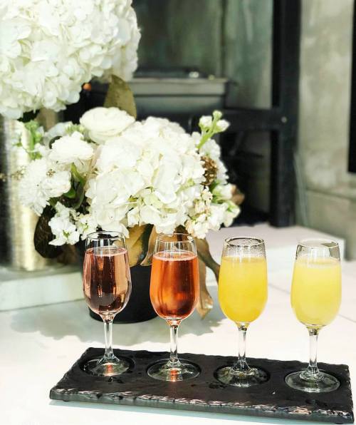 Four elegant glasses of drinks on a tray, with a bouquet of white flowers in the background.