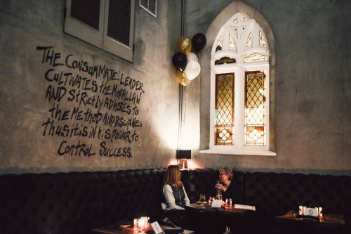 Two women sit at a table in a dimly lit restaurant with decorative walls and balloons, engaged in conversation.