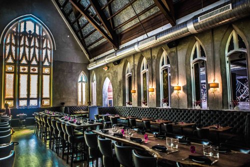 Interior of a stylish restaurant featuring high ceilings, large windows, and elegant seating arrangements.