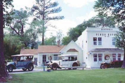 Historic buildings with vintage cars parked outside, surrounded by trees and a clear blue sky.