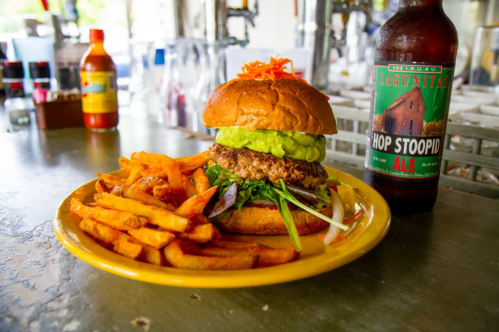 A delicious burger topped with guacamole and served with fries, alongside a bottle of Lagunitas Hop Stoopid Ale.