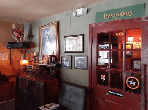 A cozy interior with a red door labeled "Restrooms," framed pictures, and a quirky statue on a shelf.
