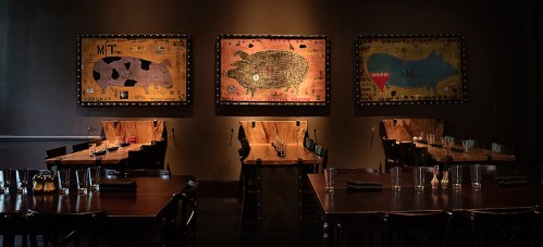 A dimly lit restaurant featuring wooden tables and three large animal-themed artworks on the walls.